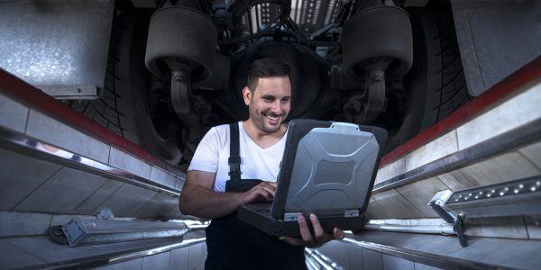Vehicle mechanic with diagnostic tool laptop working under the truck in workshop.