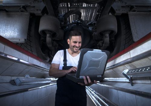 Vehicle mechanic with diagnostic tool laptop working under the truck in workshop.